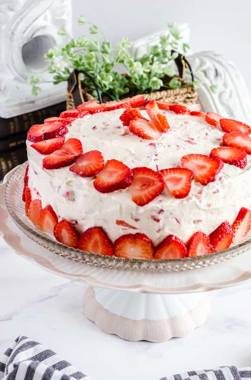 Vanilla strawberry layer cake with fresh strawberries decorating the top and sides on a cake stand.