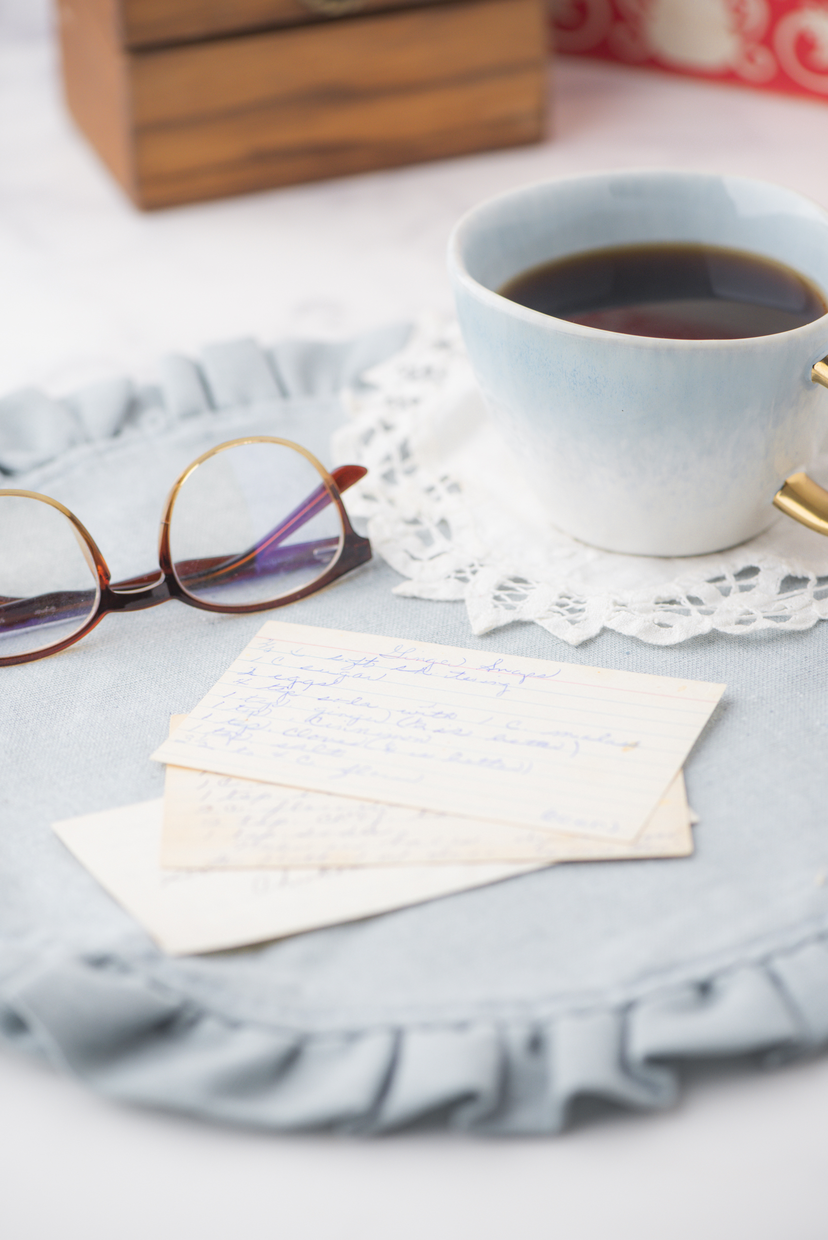 a pile of old recipe cards with a cup of coffee and pair of glasses beside it. Vintage cookbooks are in the background.