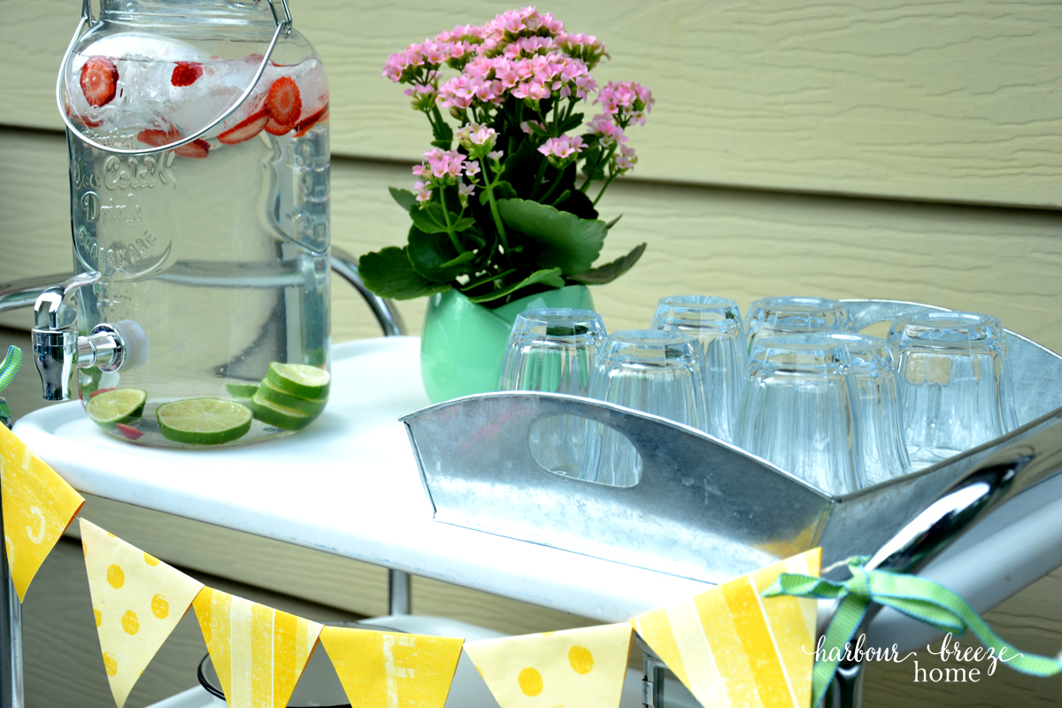 a 3 tier rolling cart set up for a bbq party with a yellow paper banner on the front
