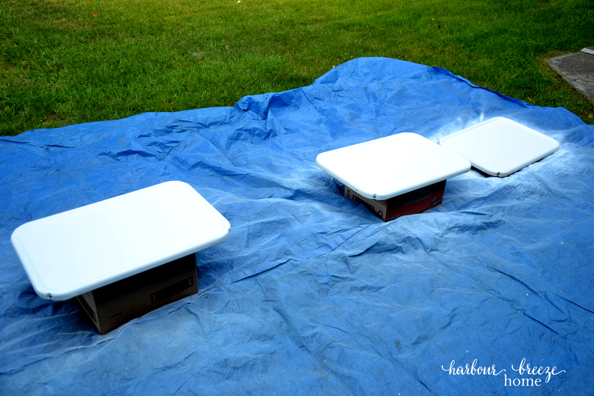 3 shelves from a 3 tier rolling cart that have been spray painted and are drying while sitting on a tarp.