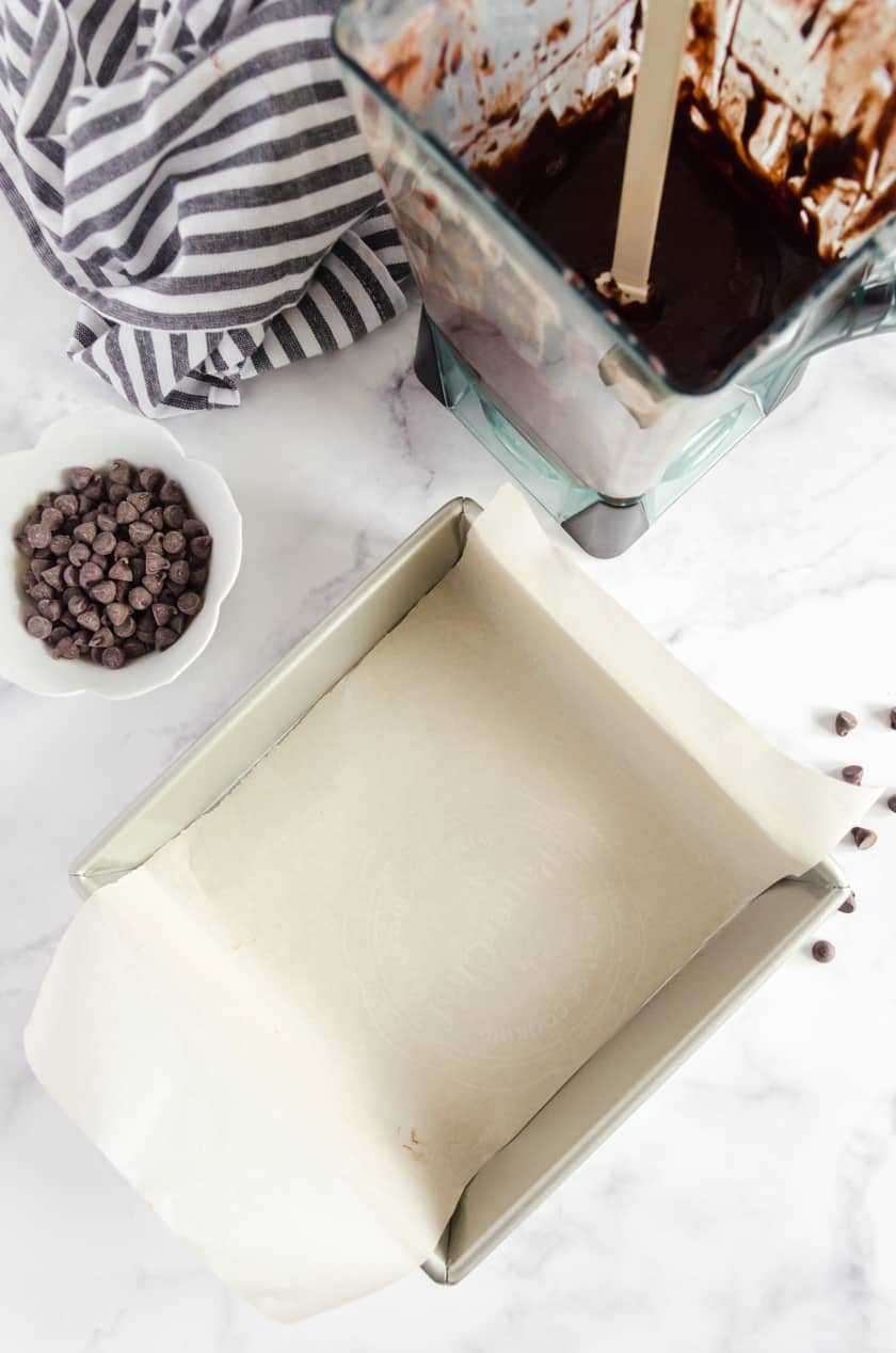 Parchment paper lining a square pan with brownie batter beside it.