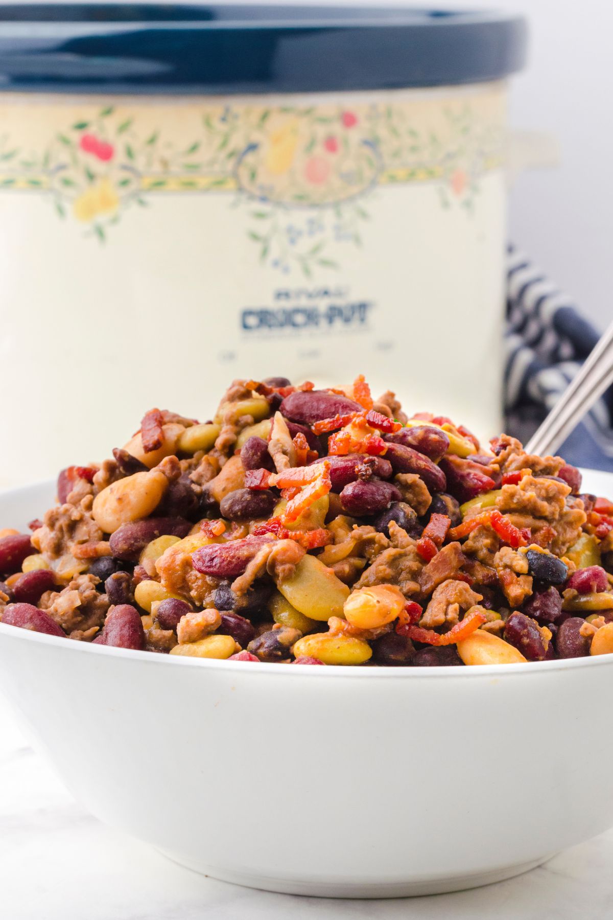 A serving dish full of crock pot baked beans with a crock pot behind it.