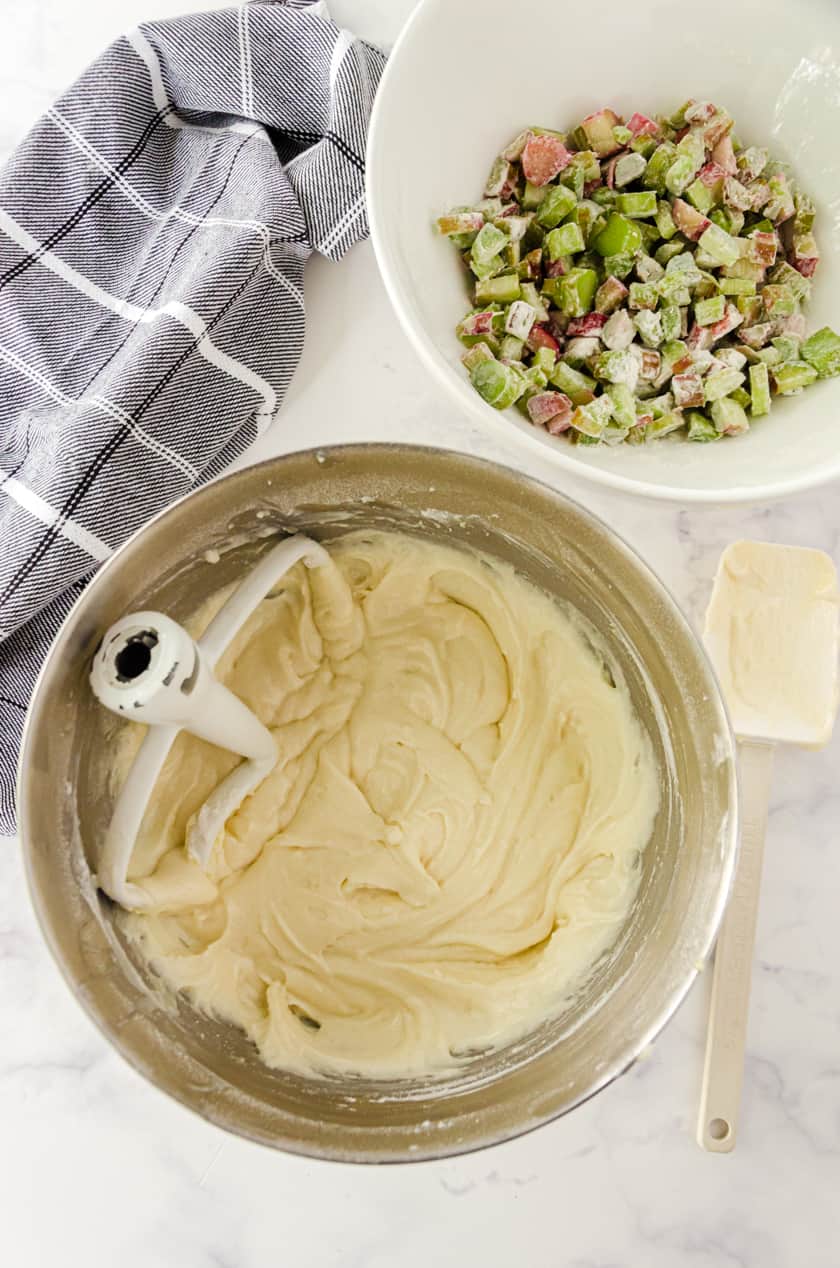 Rhubarb coffee cake batter mixed in the bowl of a stand mixer with flour covered rhubarb in another bowl.