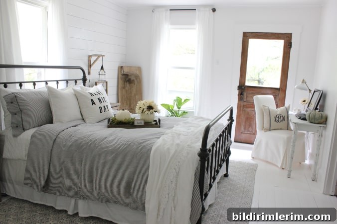 Stylish Modern Farmhouse Bedroom Ideas 10 A white farmhouse bedroom with a metal bedframe bed in black, a small table for a desk and a wooden door leading outside.