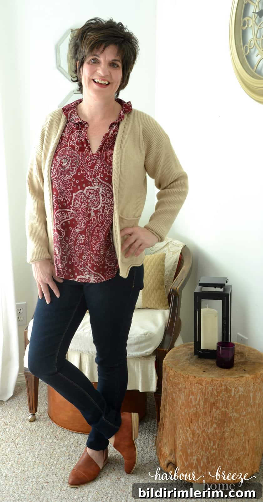 Woman standing wearing jeans, burgundy top, cream cardigan, and brown leather shoes