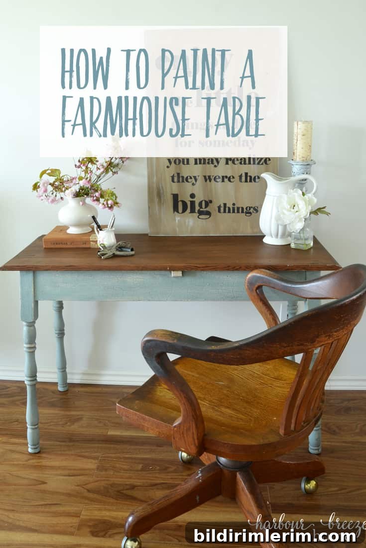 a table with wood stained top and blue legs with an antique oak office chair sitting in front of it and a bouquet of pink flowers on the top