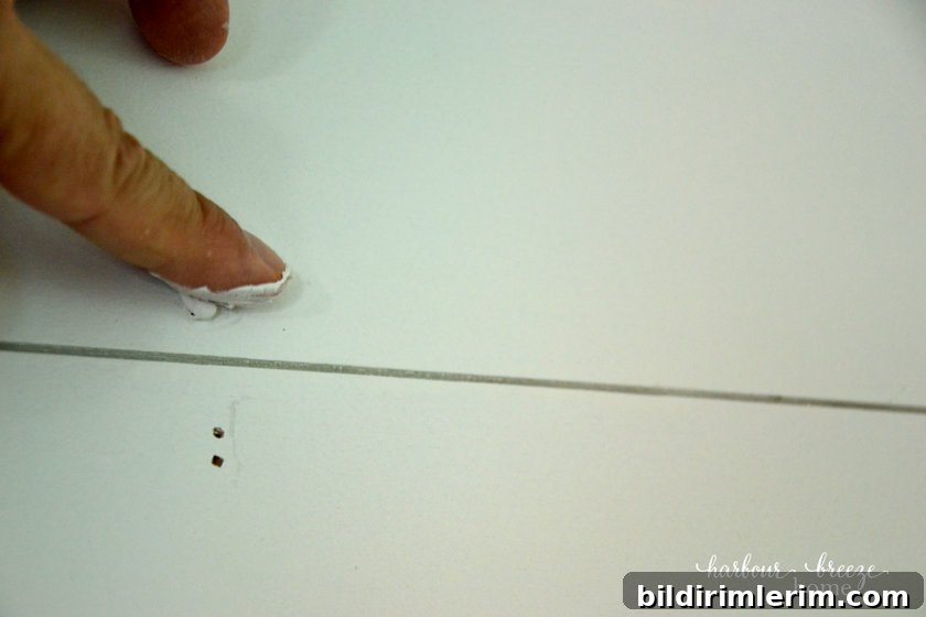 Putting dap on the nail holes with a finger as part of the process of a DIY farmhouse shiplap wall