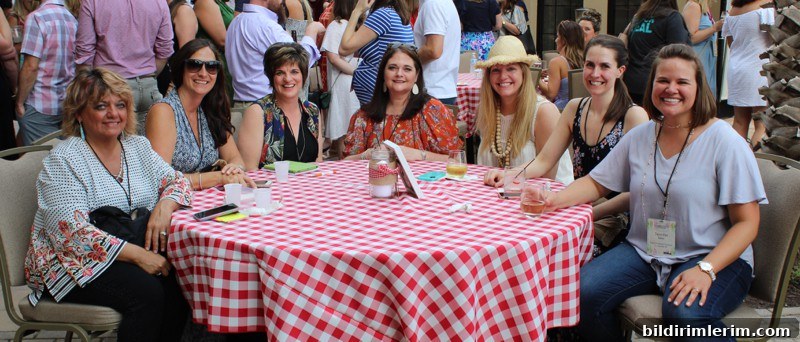 7 women sitting at an outdoor table with red checked tablecloth