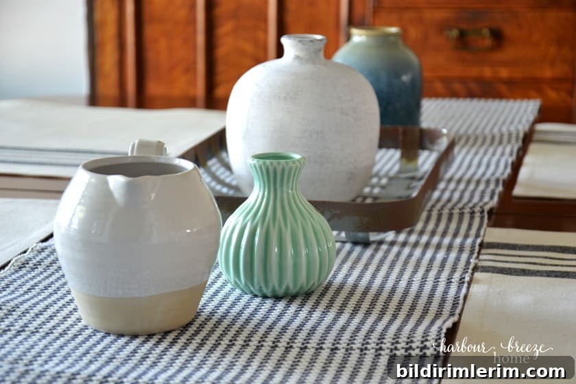 Empty vases and pitchers scattered down the center of a gray checked table runner