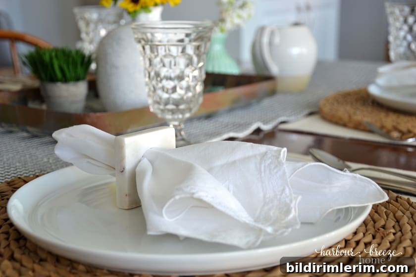 a white cloth napkin in a square napkin holder sitting on top of a white plate with a wicker charger underneath