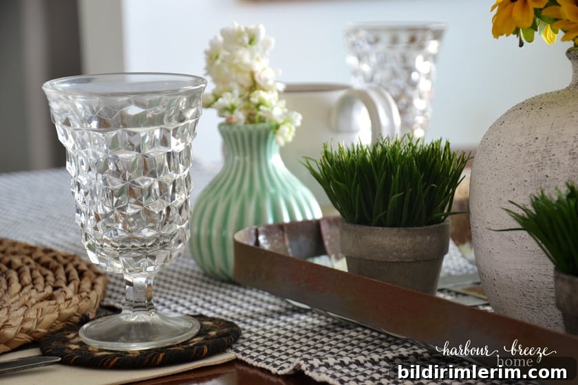 a clear glass with cut out feature set at the top of a table place setting with flowers nearby