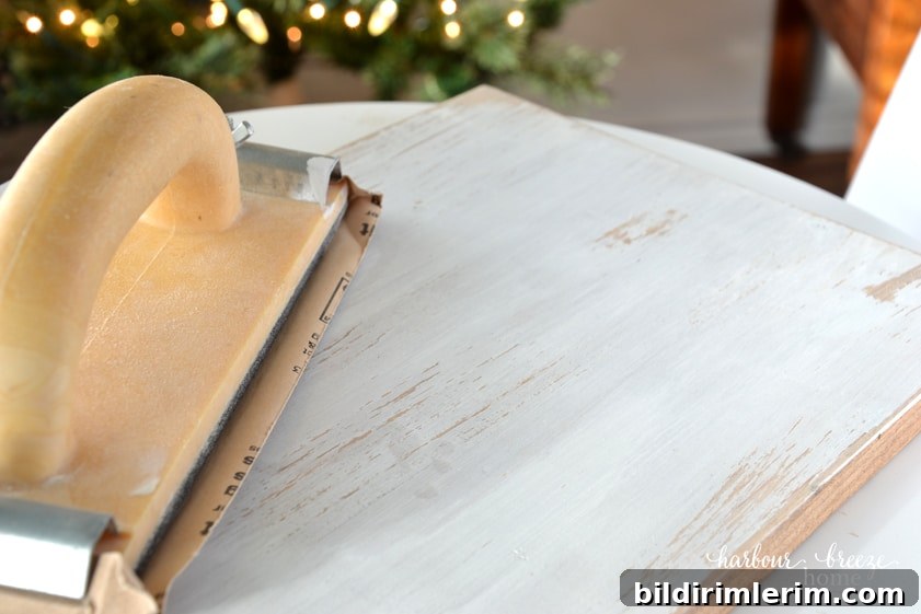 How to Make a Wood Slice Christmas Tree Sign 5 A piece of painted wood being sanded to reveal a hint of wood underneath for an aged and rustic look.