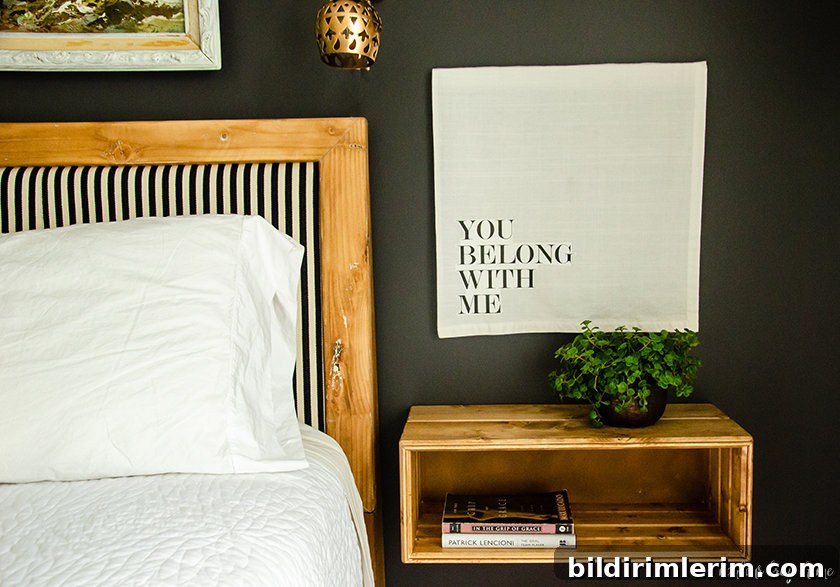 The floating bedside table completed and hung on the wall beside a bed with a plant on the top and books in the shelf.