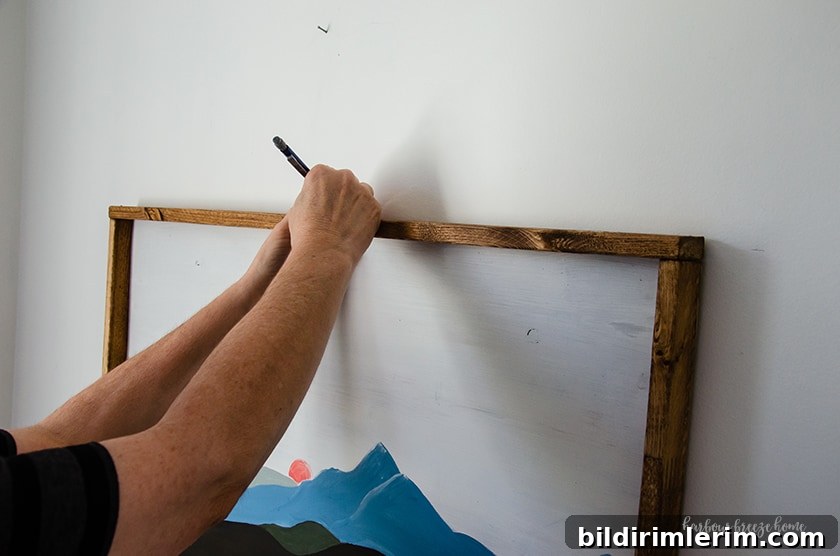 Hang a Picture on Drywall with Two Hooks: Step-by-Step Guide 5 A person holding a picture up to a white wall and marking the center placement with a pencil.