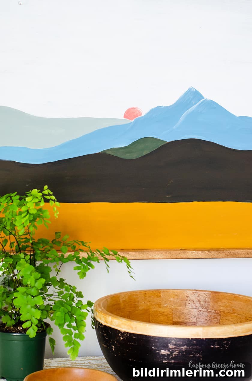 An easy mountain painting with color blocked lines with the colors yellow, black, green, blue and gray - with a pink moon peeking behind the mountain