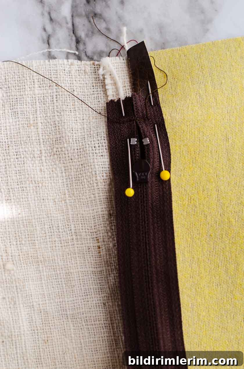 Pins holding a zipper facedown on top of the bottom seam of a faux leather pillow cover.