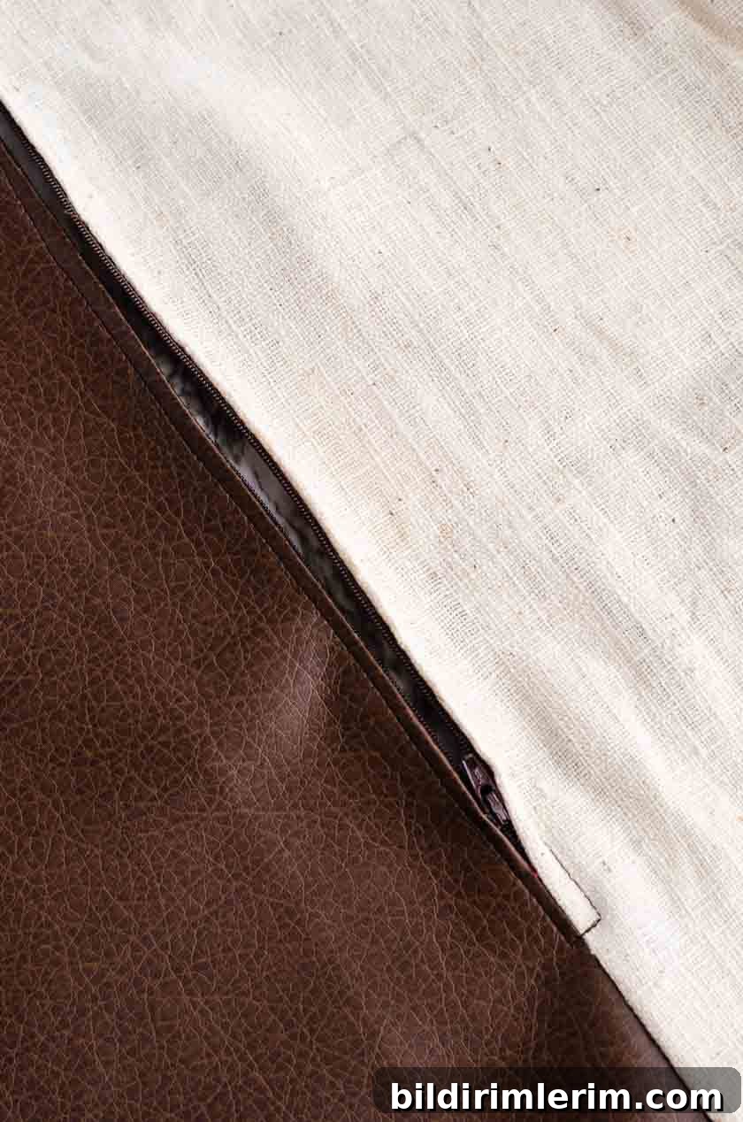 The zipper on the bottom of a faux leather pillow cover with linen back.