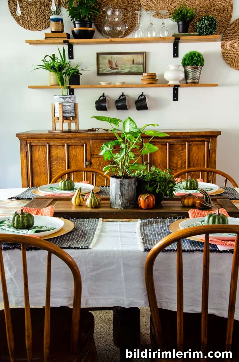 Dining room table set in a Fall decor scheme with faux pumpkins, live plants, orange checked napkins, and floral green napkins.