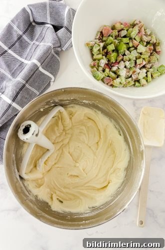 Rhubarb coffee cake batter mixed in the bowl of a stand mixer with flour covered rhubarb in another bowl.