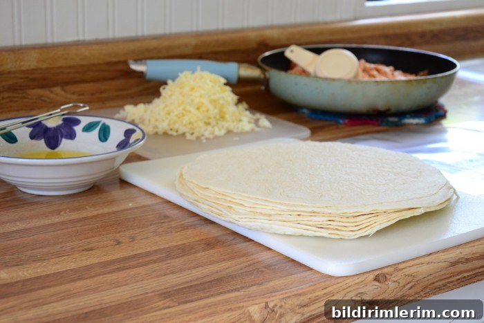 Crispy Baked Chicken Chimichangas 3 A stack of tortillas on the counter with a pan of cheese and stack of grated cheese behind it - the ingredients needed for this chicken chimichangas recipe.