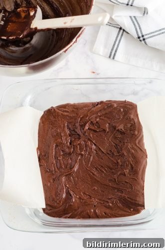 Brownie batter in a parchment lined 8x8 inch baking dish.