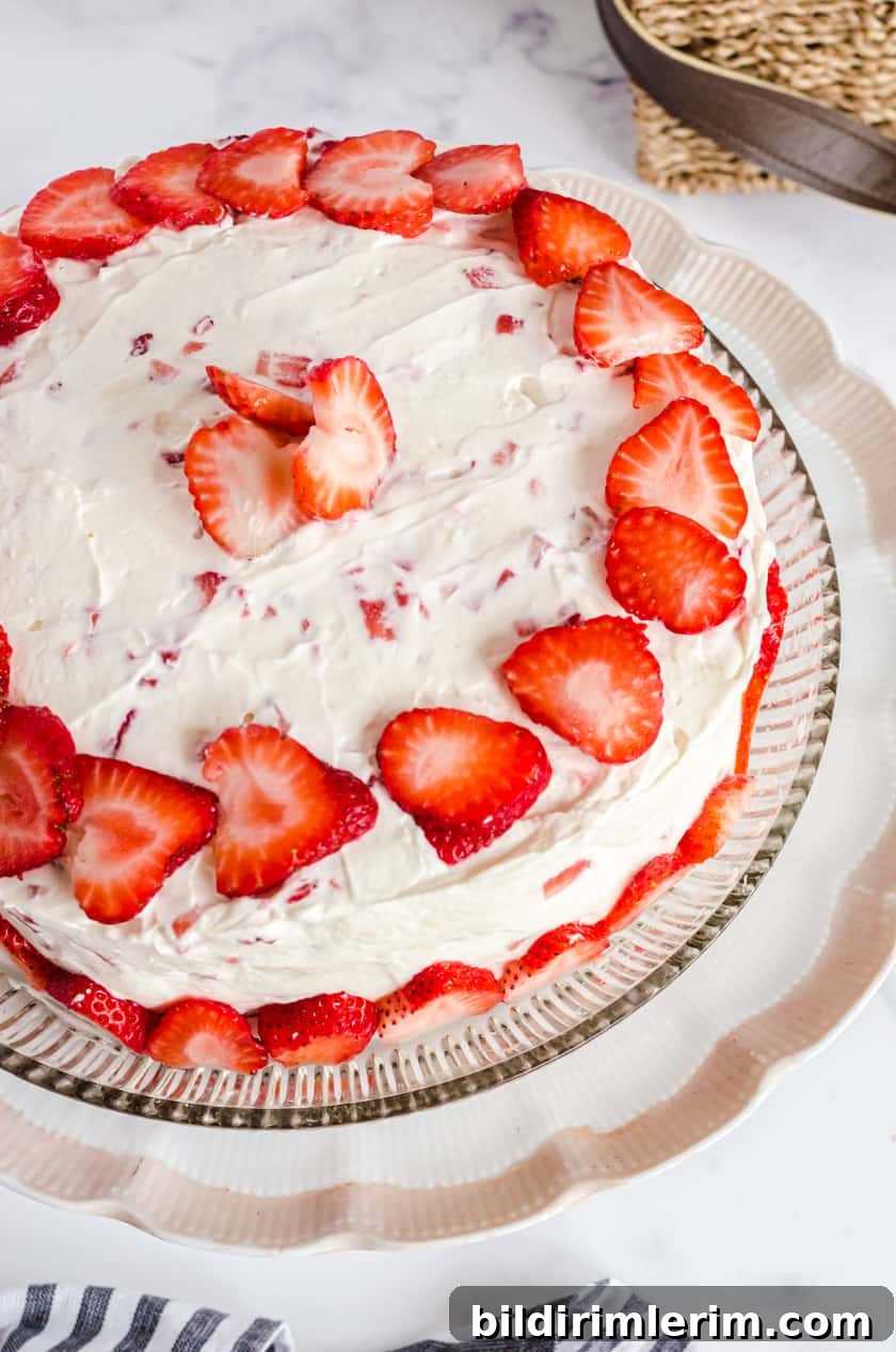 A vanilla strawberry cake with fresh strawberry icing on a cake platter.