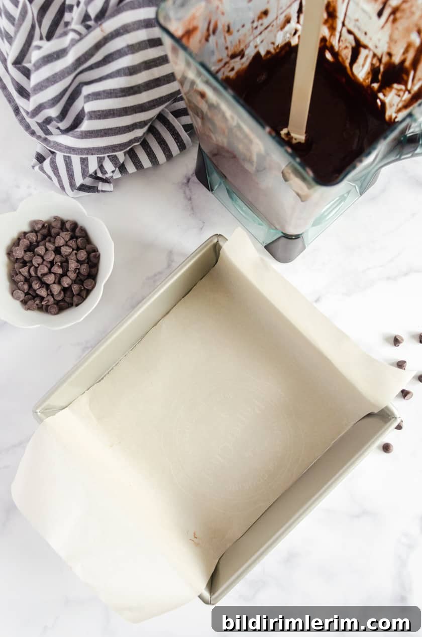 Parchment paper lining a square pan with brownie batter beside it.