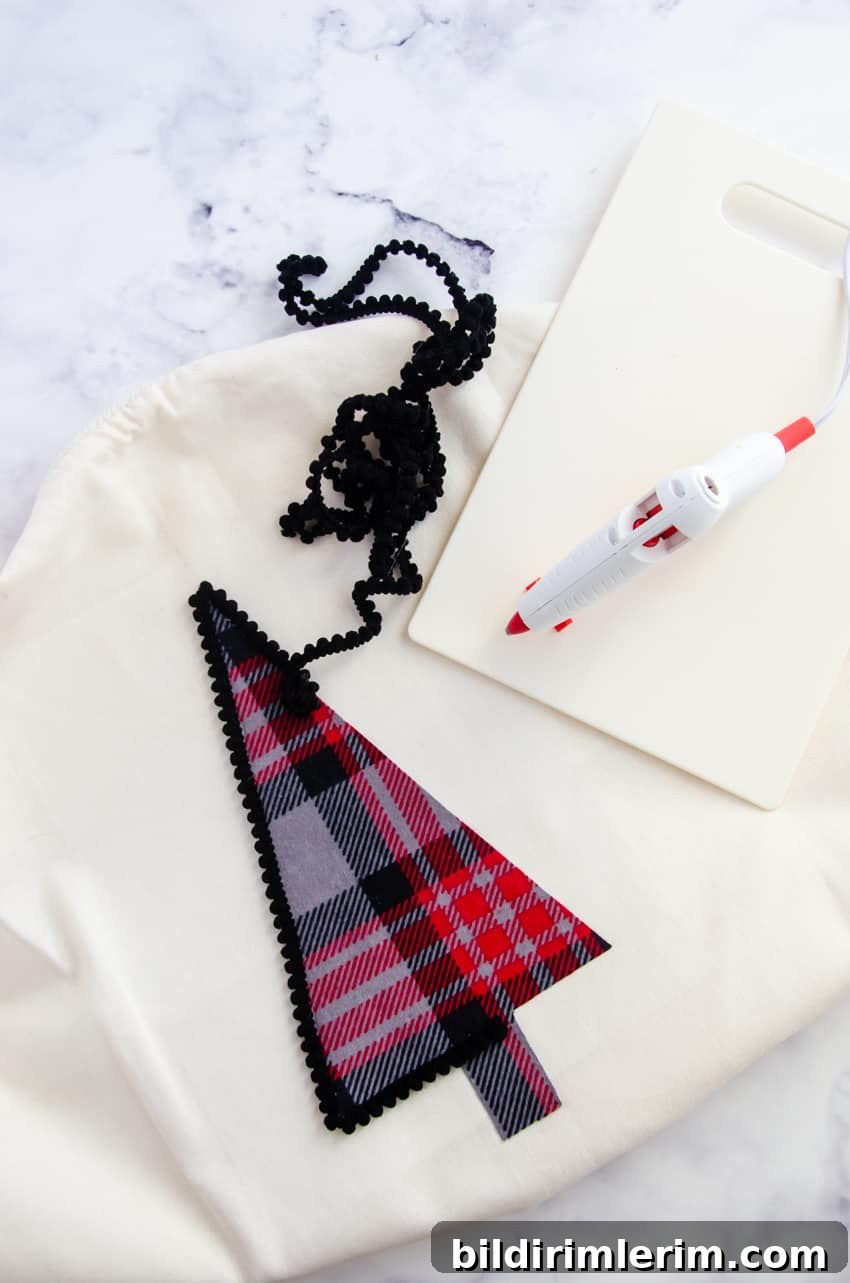 Black pom pom trim around a plaid flannel Christmas tree on a white pillow cover is a great farmhouse style DIY Christmas decor project.