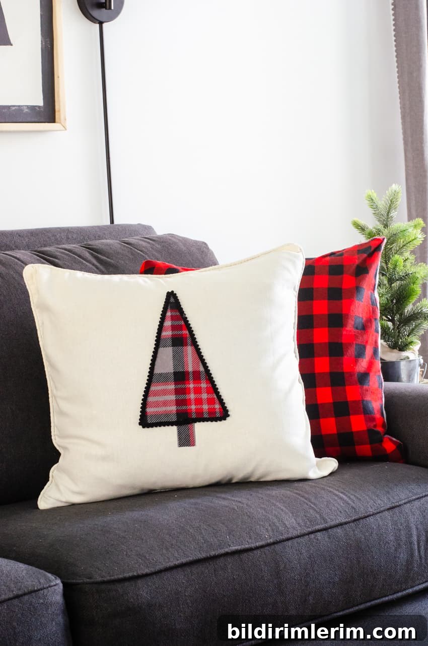 A DIY Christmas tree pillow propped up on a grey couch in front of a red buffalo check flannel pillow.