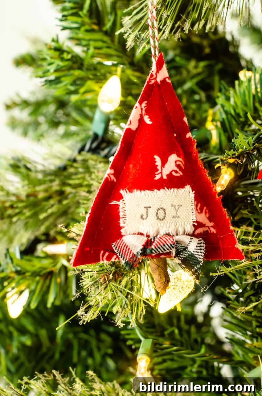 DIY Scandinavian fabric Christmas Ornament shaped like a tree with the word "joy" on it hanging in a tree.