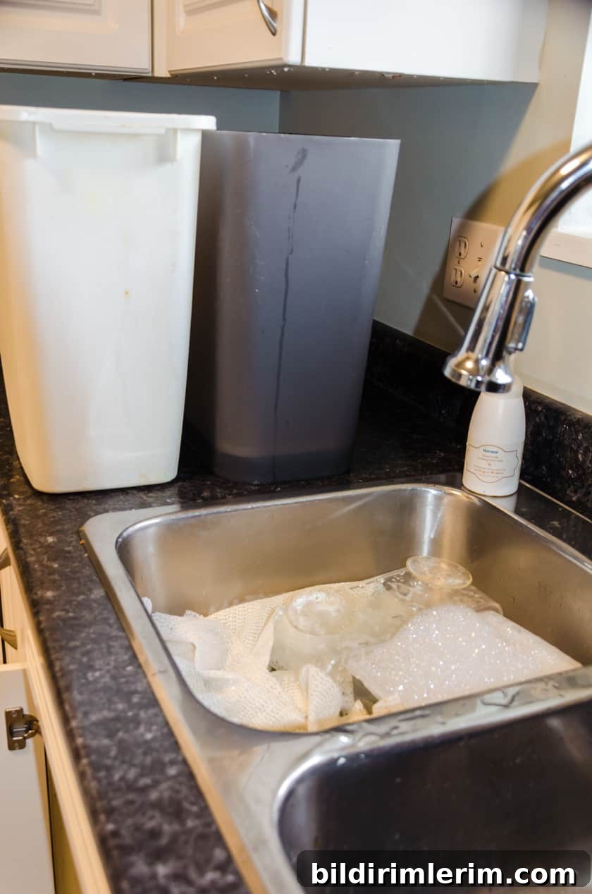 Garbage cans soaking in water and a sink full of soapy water with organizational containers in it.