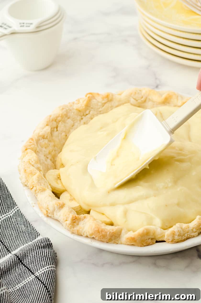 Vanilla pudding being spread over bananas in a banana cream pie shell
