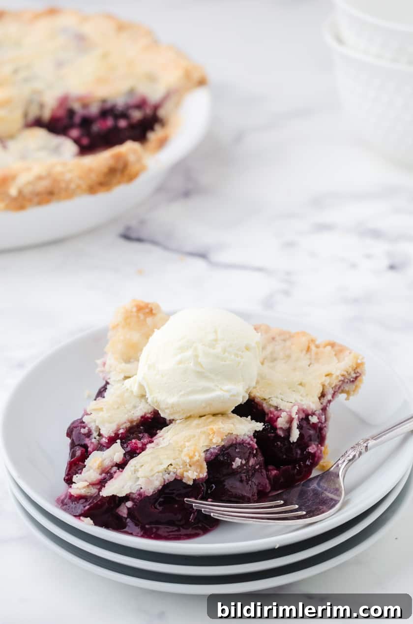 A slice of homemade cherry pie made with canned cherries with a scoop of ice cream on it.