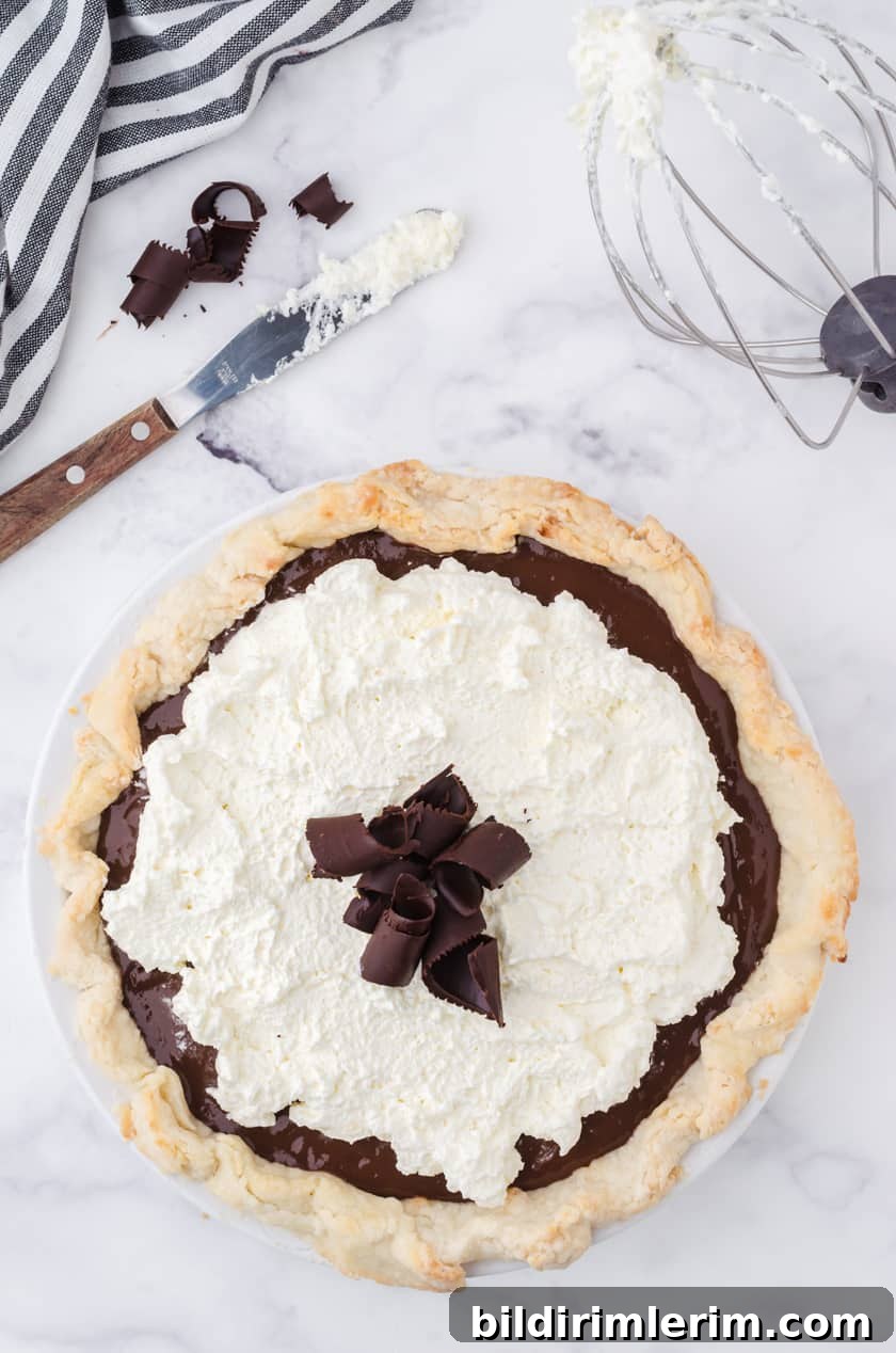A whole chocolate pudding cream pie with a mixing bowl whisk with whipping cream beside.