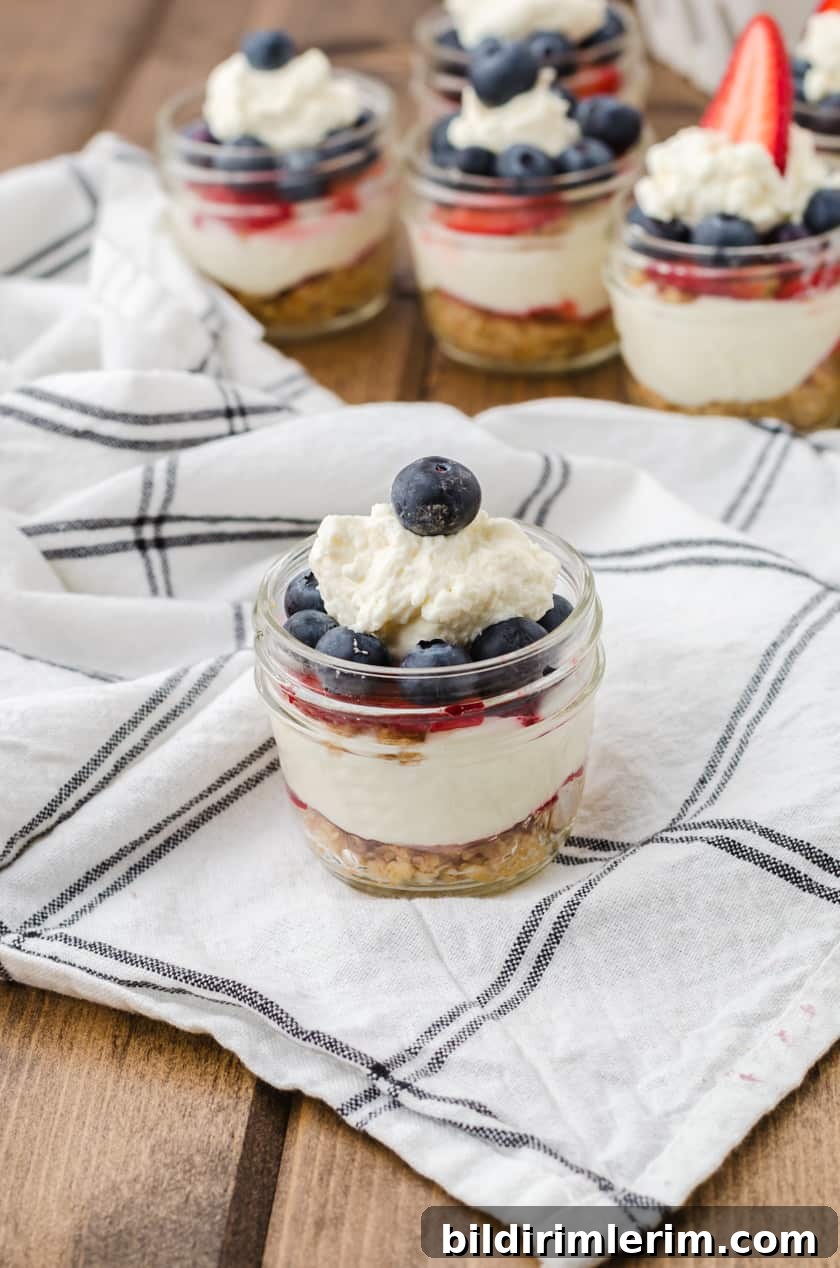 A mason jar cheesecake filled with layered no bake cheesecake with a blueberry on top.