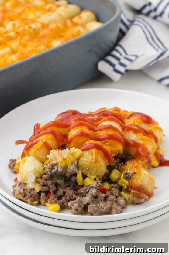 Tator tot casserole dished out on a plate with ketchup drizzled on the top.