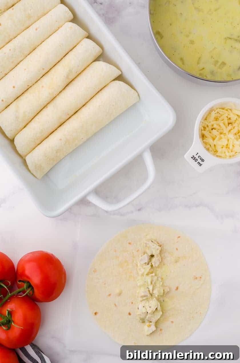 Creamy Chicken enchiladas rolled up in a baking pan with a pot with the creamy sauce beside.