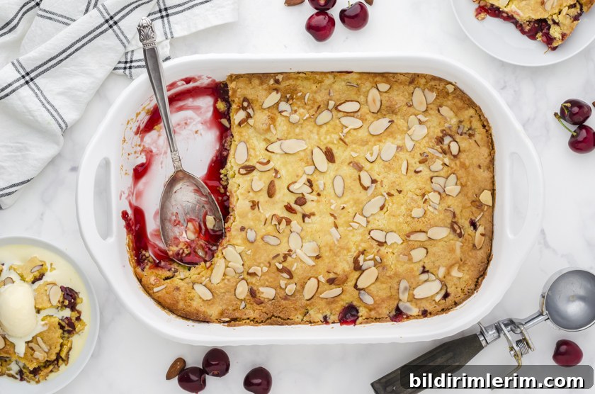 A pan of cherry dump cake with a few pieces dished out onto serving plates.