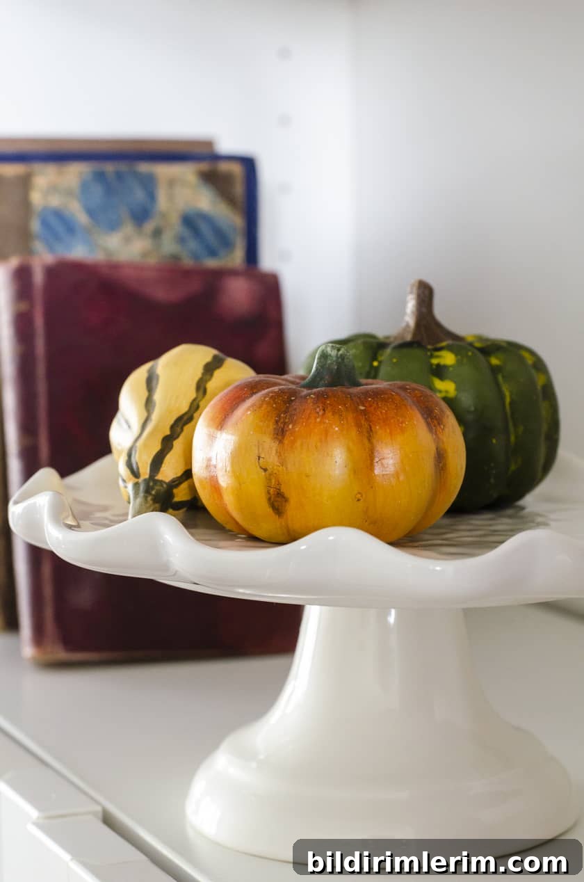 Faux pumpkins piled on a cake stand sitting in a Billy Bookcase as a Fall decor idea