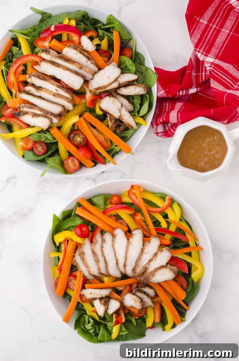 Two plates of grilled chicken salad with the pitcher or peanut chili sauce sitting beside them