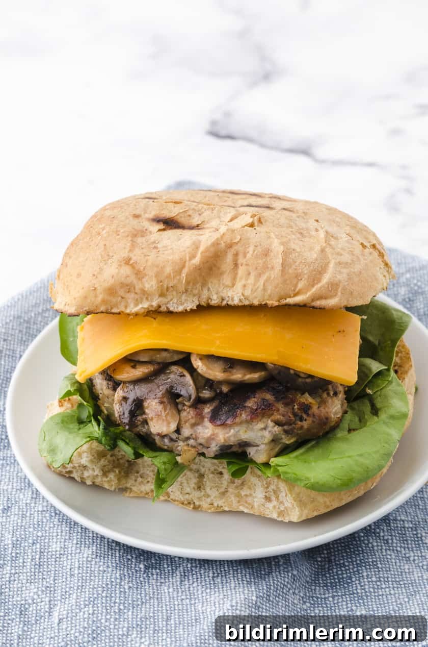 a grilled turkey burger on a plate with sauted mushrooms, lettuce, cheese and a toasted bun.