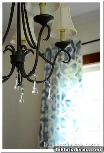Black chandelier with white lampshades with a glimpse of blue stenciled curtains hanging in the background
