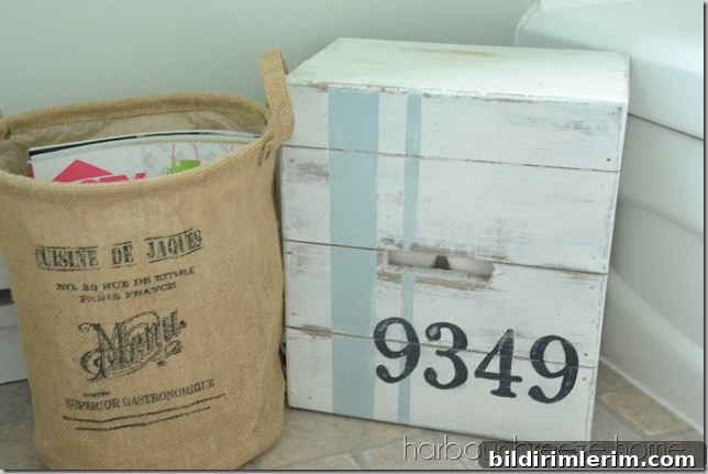 A large basket with magazines and a crate filled with toilet paper on the bathroom floor.
