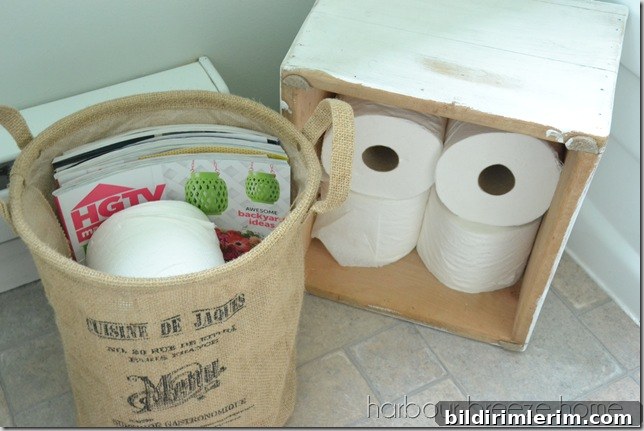Toilet paper rolls tucked into a basket and crate sitting on a bathroom floor.