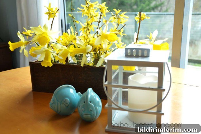 A spring decor arrangement on a tabletop with a daffodil flower arrangement, white lantern, and blue fish salt and pepper shakers