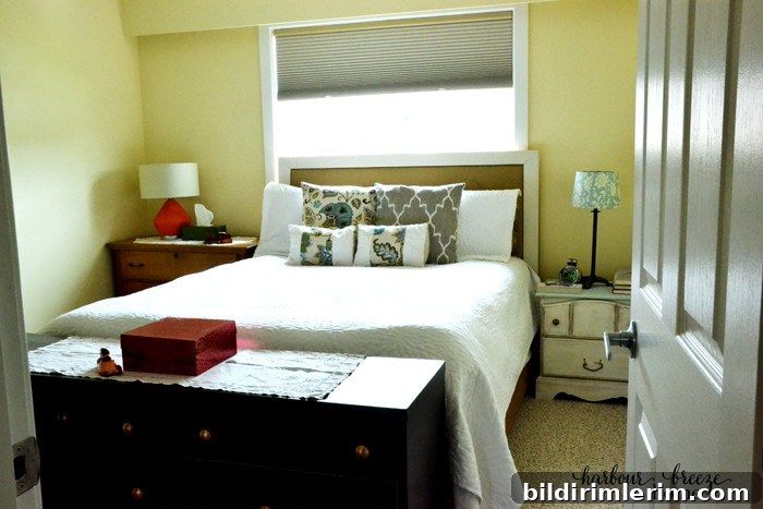 A queen bed under a window in the center of the main wall of a bedroom with a dresser on one side and a nightstand on the other. A long, low dresser sits at the foot of the bed.