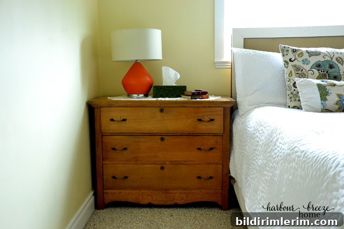 A small chest of drawers beside the bed that acts as storage and a nightstand.