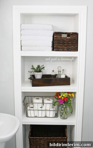 A bathroom design inspired by Joanna gaines and the farmhouse style - with a shelf unit filled with white towels, woven baskets, wooded tray, wire basket, and flowers