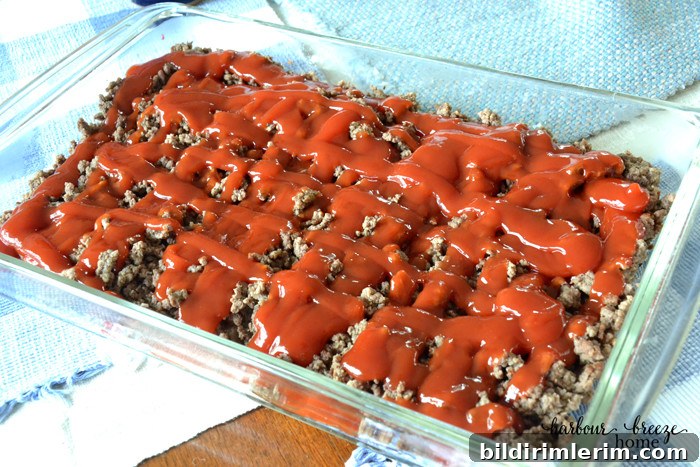 One-Pan Cheeseburger Casserole with Homemade Biscuit Topping 3 Ketchup poured over browned hamburger in a casserole dish.
