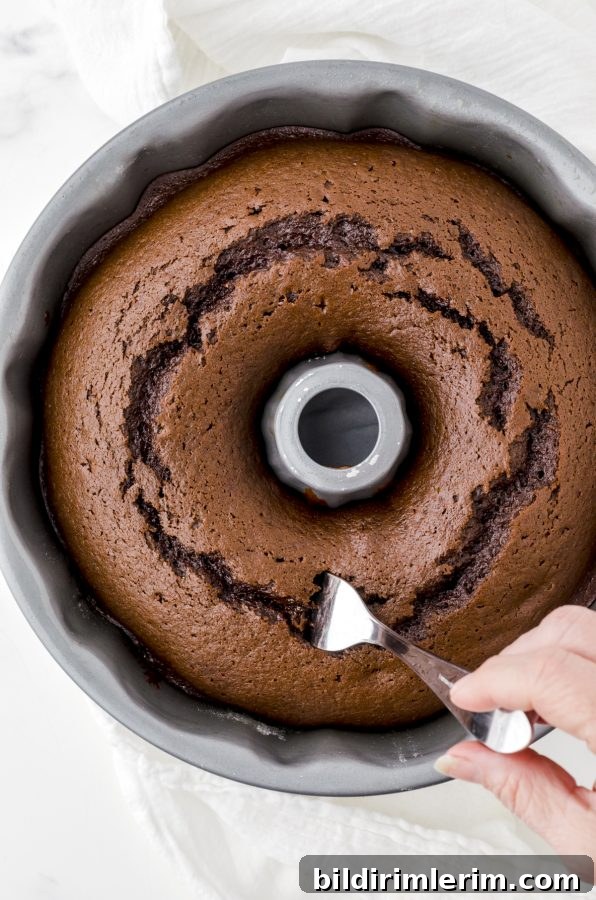 Gingerbread cake baked in a bundt pan being poked with a fork.